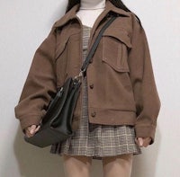 a woman wearing a brown jacket and a plaid skirt